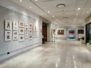 Fotografija galerije KCL Bratuz, z vhodom in številnimi slikami na stenah.