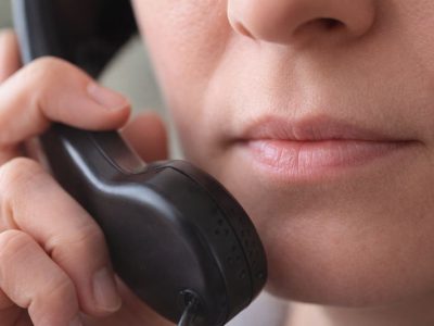 Primo piano di una persona con la bocca chiusa che tiene una cornetta telefonica vicino al viso.