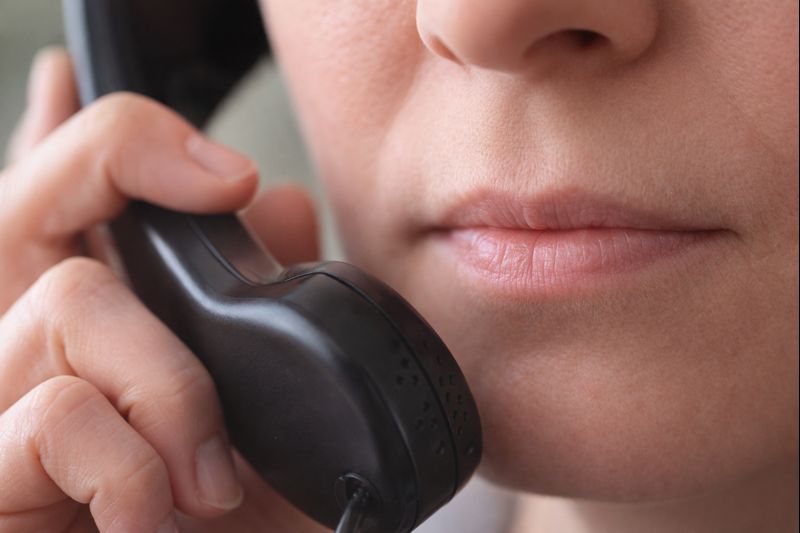 Primo piano di una persona con la bocca chiusa che tiene una cornetta telefonica vicino al viso.