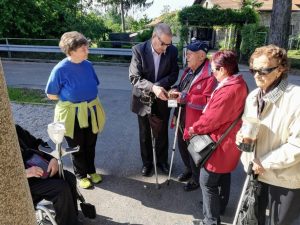 Un gruppo di persone anziane all’aperto; alcune hanno bastoni bianchi ed esplorano piccoli oggetti etnologici al tatto.