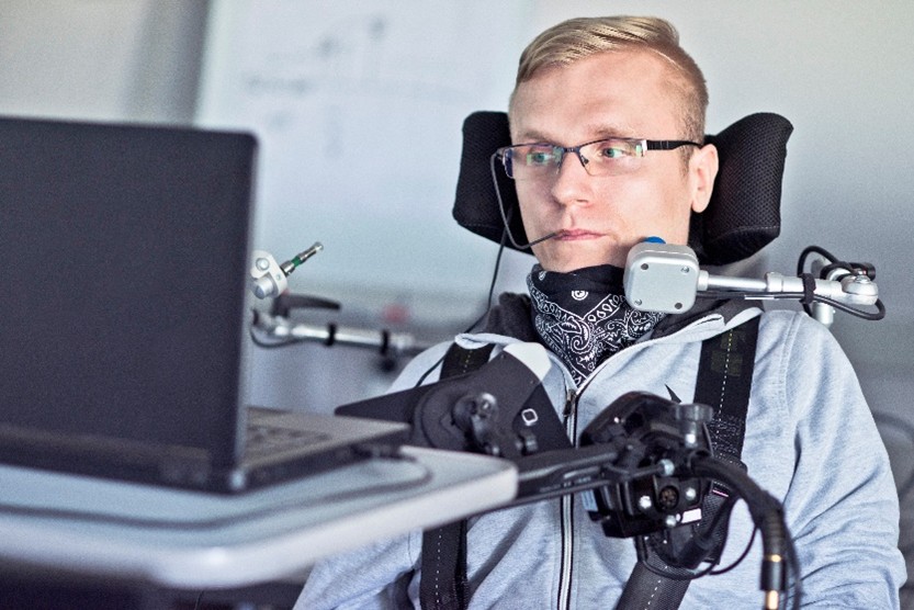 Una persona utilizza una carrozzina, interruttori e altri dispositivi assistivi per usare il computer.