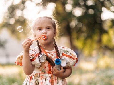 Una bambina all'aperto soffia bolle di sapone e tiene in mano un contenitore con la soluzione.