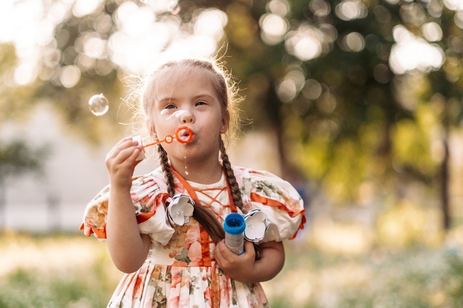 Una bambina all'aperto soffia bolle di sapone e tiene in mano un contenitore con la soluzione.