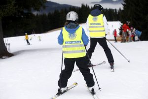 Sciatore con un gilet di sicurezza giallo recante la scritta «Sciatore ipovedente» mentre scia su una pista innevata accompagnato da una guida.