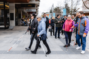Più persone con bastone bianco attraversano una strada cittadina seguendo i percorsi tattili durante un'attività di orientamento e mobilità.