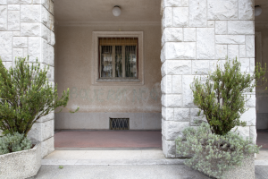 I pilastri d’ingresso del palazzo municipale di Nova Gorica, con una finestra dotata di inferriate tra di essi e due arbusti in fioriere davanti.