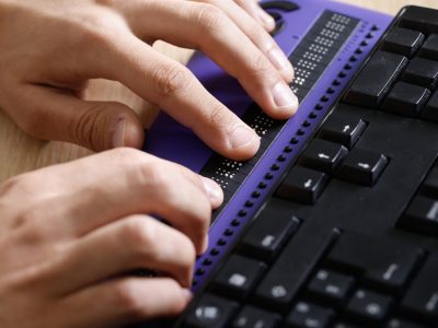Una persona legge il contenuto tramite un display Braille collegato a una tastiera del computer.