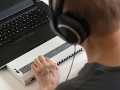 Persona utilizza una barra Braille collegata al computer per leggere e navigare nei contenuti digitali.