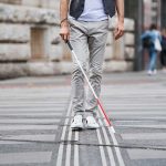 Una persona con bastone bianco segue il percorso tattile durante l'attraversamento della strada.